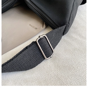 Détail du sac en toile noire montrant la boucle métallique argentée et la fermeture éclair