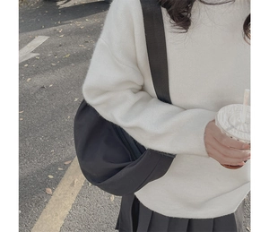 Close-up of black crescent shoulder bag with wide strap on model in casual outdoor setting