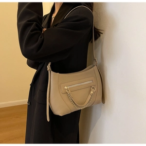 Detail view of large beige tote bag with golden chain and zip pocket on model's shoulder
