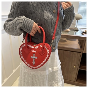 Detail of red heart-shaped bag featuring white flame print and cross charm in a home setting