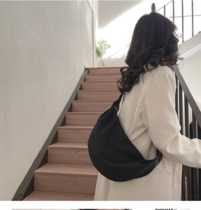 Detail of a large black crescent crossbody bag worn by a model on a minimalist staircase