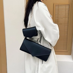 Minimalist black leather envelope crossbody bag with gold chain strap on female model