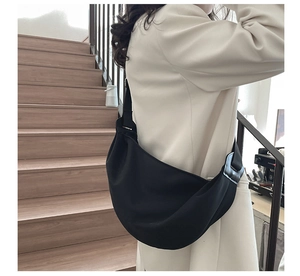 Side view of a black crescent shoulder bag with a wide strap on a female model