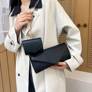 Close-up of black envelope crossbody bag set with gold chain on model in trench coat