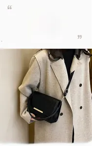 Detail of black crossbody bag with gold metal trim worn over a beige coat