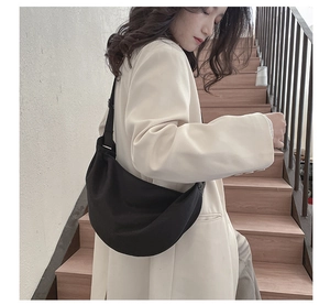 Minimalist black crescent crossbody bag with adjustable wide strap shown on model