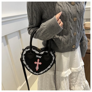 Detail view of heart-shaped crossbody bag with white artistic lettering and red cross motif