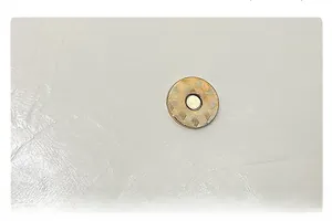 Detail of light gold magnetic clasp with geometric texture on white lychee leather bag