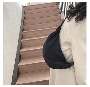 Detail of minimalist black crescent crossbody bag worn over a beige coat for daily commute
