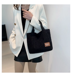 Detail of black corduroy tote bag showing the brown leather label and soft ribbed texture