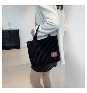 Detail of black corduroy tote bag showing textured fabric and leather fashion logo