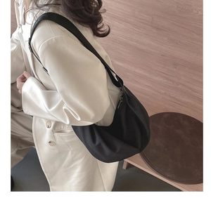 Side view of a black crescent nylon shoulder bag on a model in a white blazer