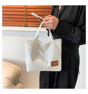 Detail of white corduroy tote bag showing vertical ribbed texture and fashion leather patch