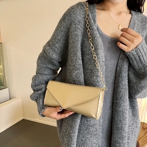 Detailed side view of a champagne envelope clutch bag with a sleek gold chain strap