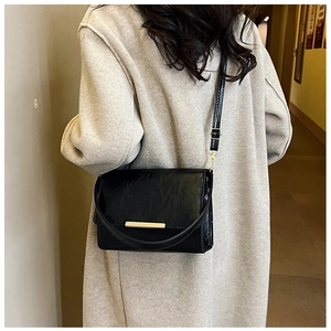 Detail of black crossbody bag featuring pleated texture and golden metal bar decoration