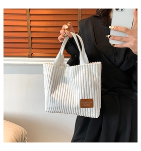 Detail of white corduroy tote bag showing ribbed texture and fashion leather tag