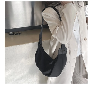 Detail of adjustable strap and crescent shape of a black nylon shoulder bag for women