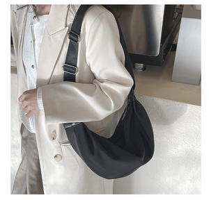 Detail of black pleated crossbody bag with wide strap and silver metal buckles