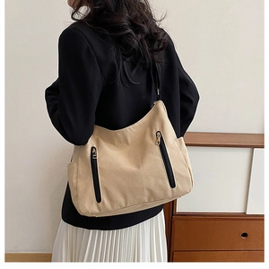 Détail du grand sac cabas en toile beige avec fermetures éclair noires porté à l'épaule