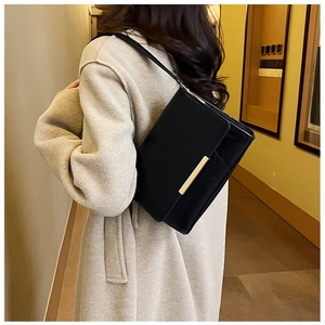 Detail of a minimalist black leather crossbody bag with elegant gold metal trim bar