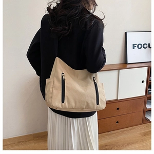 Détail d'un sac cabas en toile beige avec zips noirs et poches latérales dans un décor intérieur