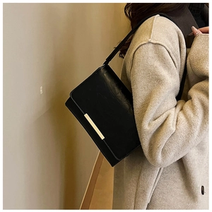 Close-up of a black leather crossbody bag with a gold buckle worn on a textured coat