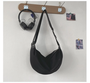 Minimalist black crescent nylon shoulder bag hanging on a wooden wall hook with headphones