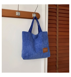 Close-up of blue corduroy tote bag featuring vertical texture and leather logo patch