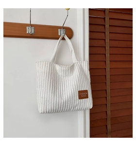 Detail of white corduroy tote bag showing textured fabric and brown leather fashion patch