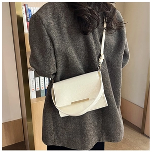 Detail of vintage textured white crossbody bag with gold metal clasp on gray wool coat