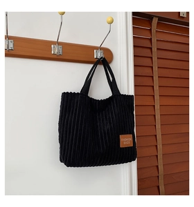 Detailed texture of black corduroy tote bag with brown fashion label on wood hanger