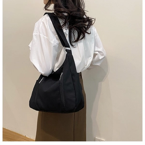 Détail d'un sac bandoulière en toile noire montrant la large sangle et la fermeture