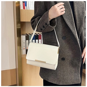 Detail of white embossed leather handbag with gold metal bar worn by model in a blazer
