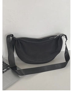 Minimalist black nylon crescent shoulder bag with metal zipper on a grey desk setup