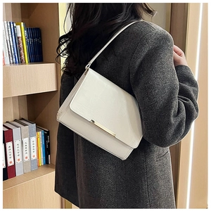 Detail of off-white crossbody bag with gold metal trim worn over a grey herringbone blazer