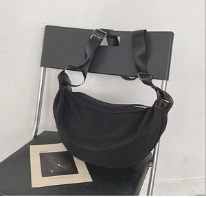 Detail of minimalist black crescent crossbody bag with adjustable wide strap on a chair