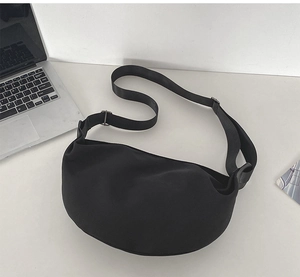 Detail of minimalist black nylon crescent bag on a white desk for office commute