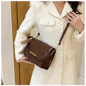 Detail of dark brown crossbody bag with glossy wrinkled texture on tweed jacket