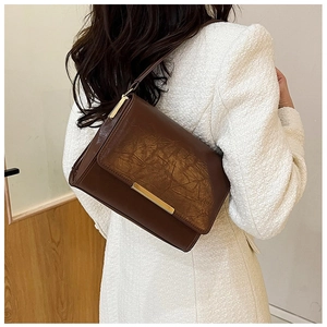 Detail of vintage dark brown crossbody bag with retro texture and gold buckle on white coat