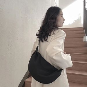 Minimalist black crescent crossbody bag with wide shoulder strap worn by a female model