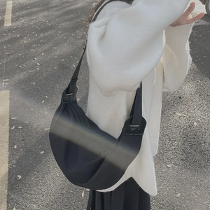 Minimalist black crescent crossbody bag with adjustable wide strap shown on a model outdoors