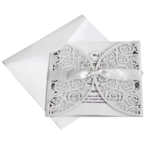Elegant white laser-cut rose wedding invitation with a silk bow and matching envelope