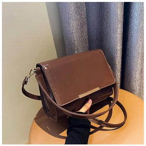 Detail of brown glossy leather crossbody bag with a sleek gold metal trim on bottom