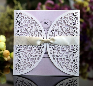 Detail of white laser-cut leaf wedding invitation with pink insert and ribbon bow