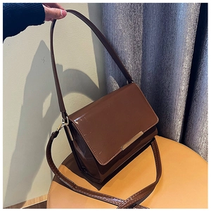Detail view of a brown glossy patent leather crossbody bag with gold metal hardware