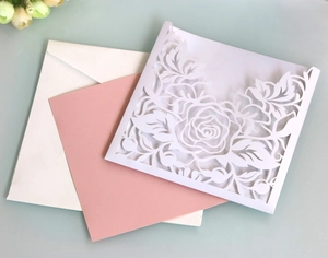 Close-up of laser-cut white floral wedding invitation with pink insert and matching envelope