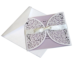 Detail of white laser cut leaf lace wedding invitation with lavender card and satin bow