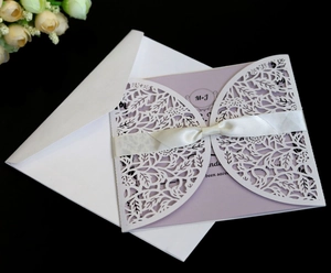 Detail of white laser-cut leaf pattern invitation cover with purple card and satin bow