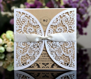 Detail of laser-cut lace wedding invitation with white ribbon bow and kraft paper insert