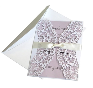 Detail of laser-cut white floral lace invitation with silk bow and pink inner card